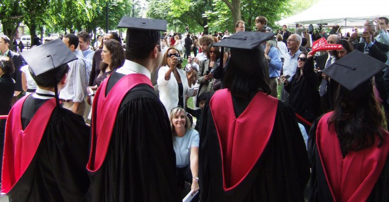 four graduates posing with cap and gowns while parents take photos in a crowd