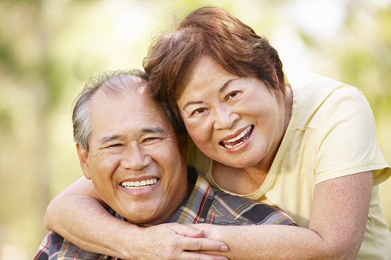 older couple asian couple embracing outside with blurred foliage