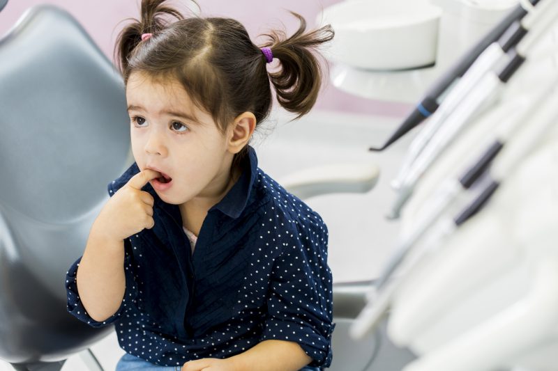 young girl in operatory pointing at her tooth with worries expression