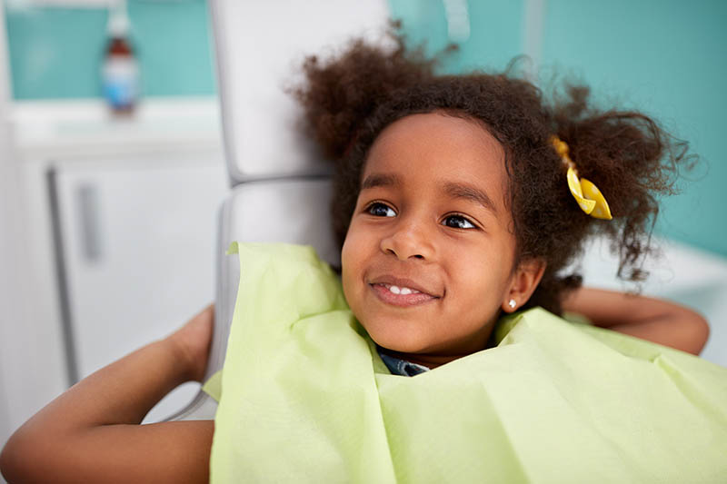 child in dental chair smiling with bib on