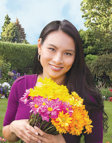 asian woman in a park holding a bouquet of flowers in both hands, smiling