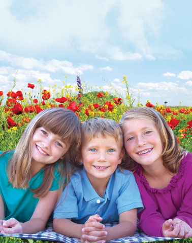 three caucasian kids sitting in a field one boy and two girls