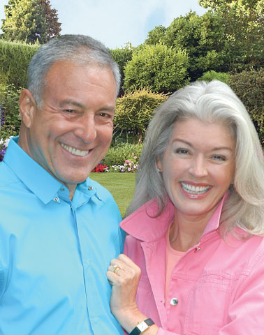 older caucasian couple in a park with flowers smiling
