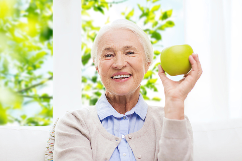elderly woman smiling holding a green apple on the balcony sitting
