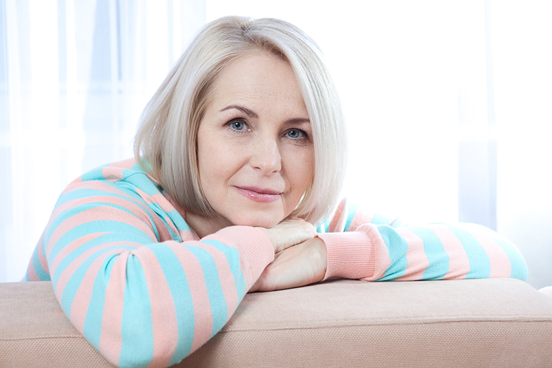 older woman smiling while sitting with arms draped over the back of a couch