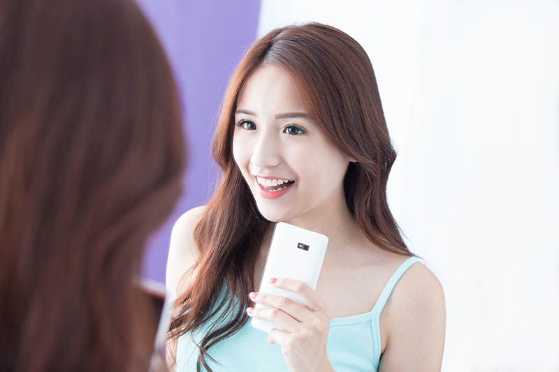 asian woman smiling holding a cell phone while talking to another woman