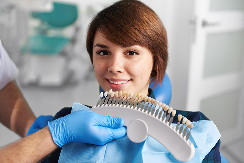 woman sitting in operatory chair while dentist with latex gloves holds a tooth shade guide