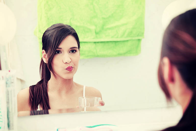brunette woman rinsing her mouth looking in the bathroom mirror