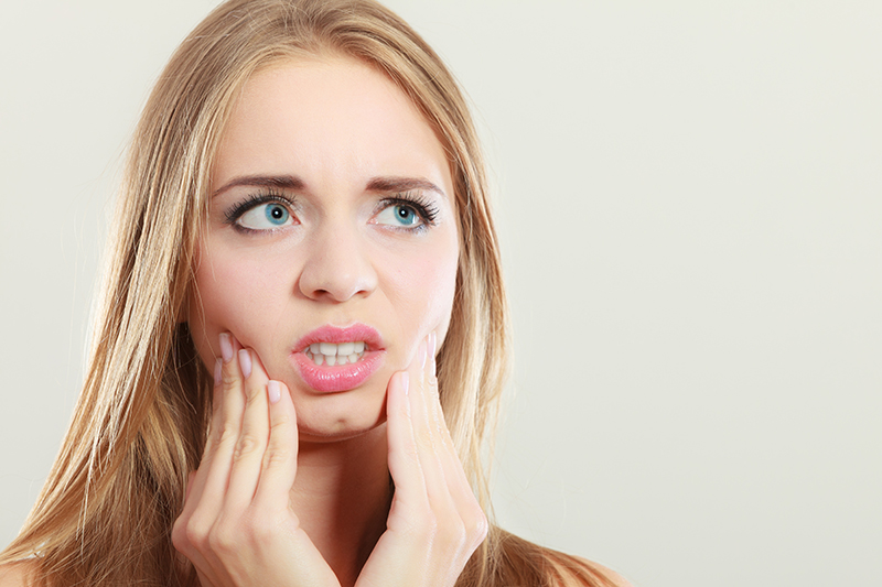 young blond woman with expression of pain holding her lower jaw with both hands